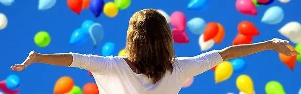 femme bras ouverts devant une nuée de ballons multi-colores