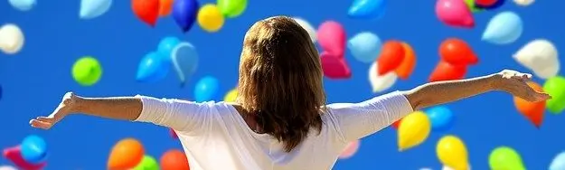 femme bras ouverts devant une nuée de ballons multi-colores